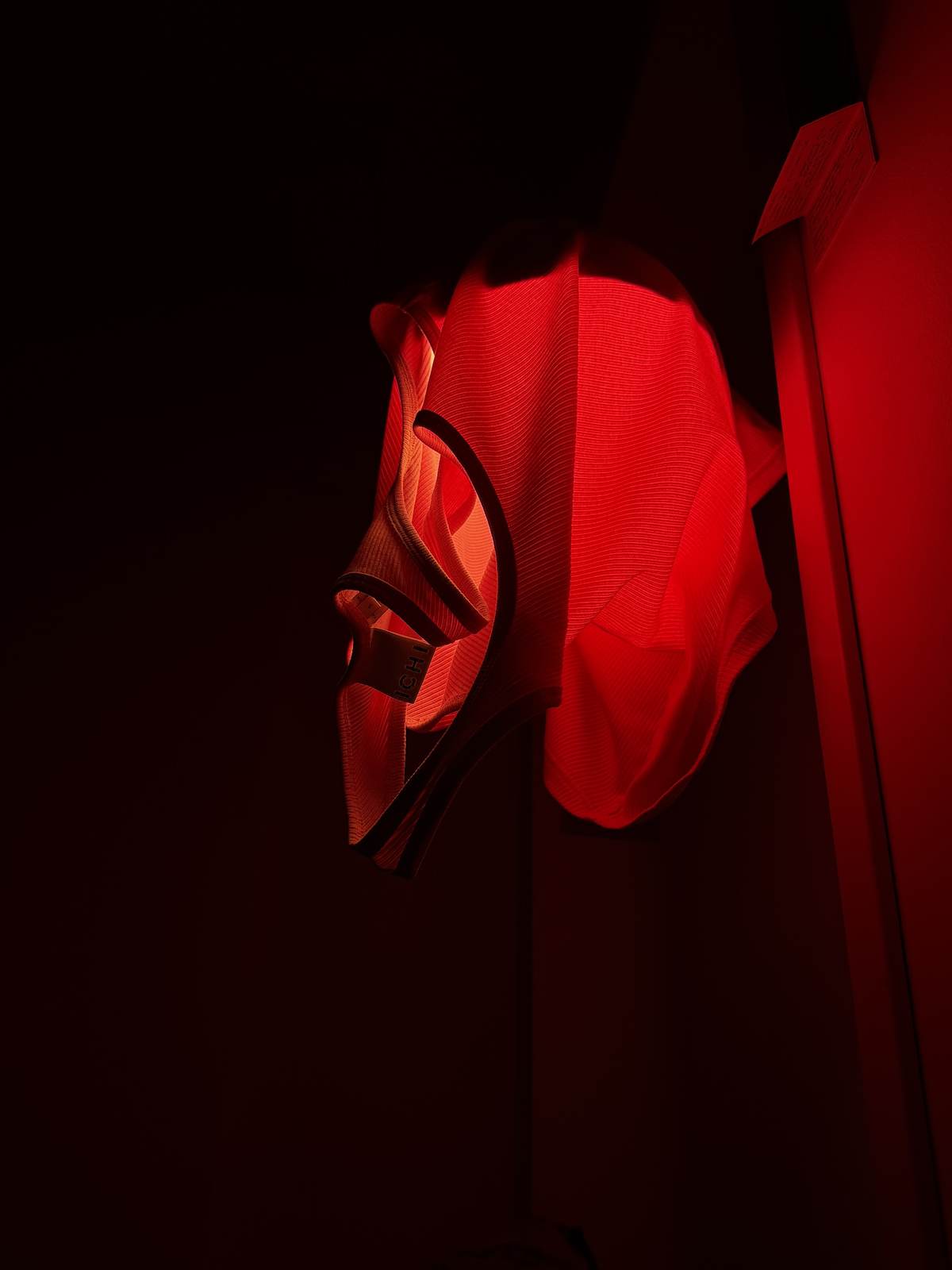 a ribbed white garment hanging in the dark, lit hard by a red lamp